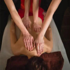 Dua orang terapis sedang memberikan pijatan sinkron pada punggung pelanggan secara bersamaan di Zavra Massage.